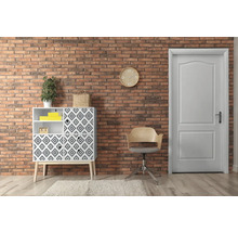 Woonkamer met commode, stoel en deur voor een bakstenen muur.
