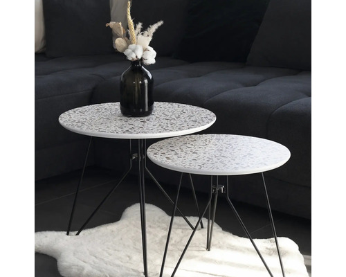 Twee ronde bijzettafels met terrazzo patroon en zwarte metalen poten staan op een kleed.