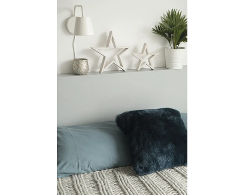 Decoratieve scène met kussens, sprei, lamp, theelichthouder, sterren en potplant op een plank