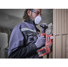 Man met ademhalingsmasker en veiligheidsbril werkt met een Einhell sleuvenfrees aan een muur.