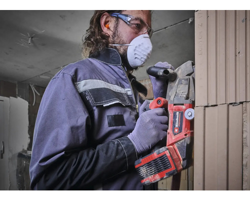 Man met ademhalingsmasker en veiligheidsbril werkt met een Einhell sleuvenfrees aan een muur.