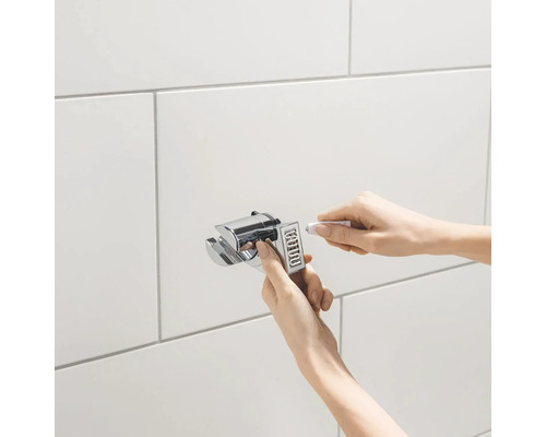 Installatie van een douchehouder met een tube afdichtmiddel op een betegelde wand.