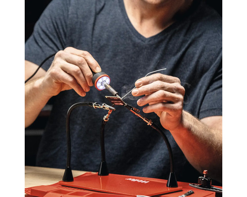 Persoon soldeert met een soldeerstation op een werkblad.