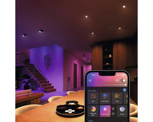 Overzicht van een woonkamer met plafondlampen, trap en een smartphone-app voor lichtregeling.