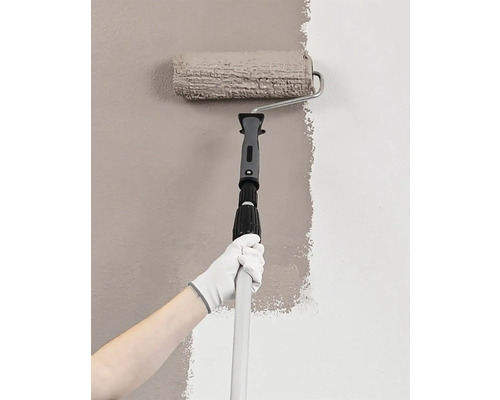 Persoon schildert muur met verfroller en telescopische steel