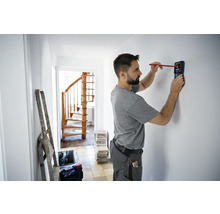 Man gebruikt een detector om objecten in een muur in een huis te vinden.