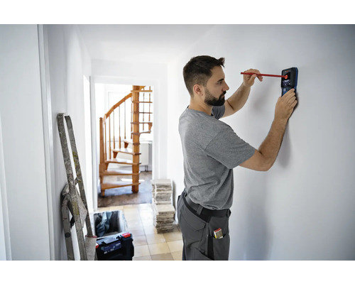 Man gebruikt een detector om objecten in een muur in een huis te vinden.