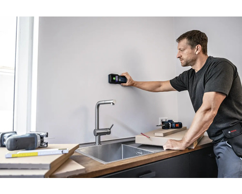 Man gebruikt een digitale detector op een muur in een keuken.