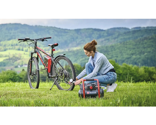 Vrouw pompt fietsband op met een Einhell compressor op een grasveld voor een heuvellandschap