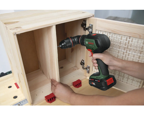 Iemand boort een houten meubel in elkaar met een accuschroefboormachine.