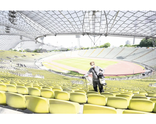 Een persoon desinfecteert stoelen in een stadion met een spuitapparaat.