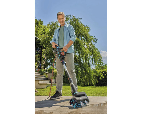 Een man gebruikt een Gardena borstel om een terras schoon te maken.