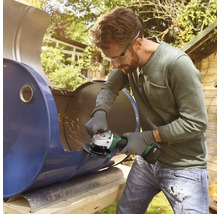 Man snijdt een metalen vat in de tuin met een haakse slijper