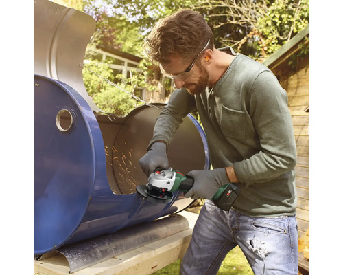 Man snijdt een metalen vat in de tuin met een haakse slijper