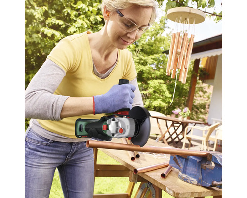 Vrouw snijdt koperen buizen in de tuin met een haakse slijper.