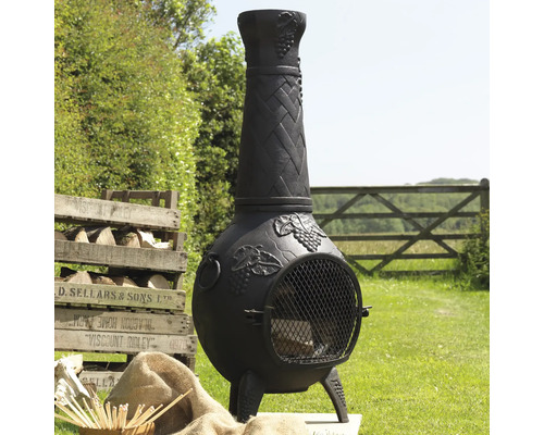 Zwarte gietijzeren terrasverwarmer met hout en houten kist in de tuin.