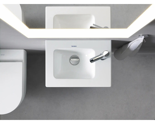 Bovenaanzicht van een badkamer met wastafel, spiegel met verlichting, handdoek en toilet.