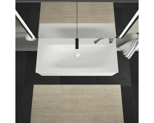 Bovenaanzicht van een badkamer met wastafel, kraan, handdoek en badmatten