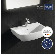 Keramische wastafel met kraan tegen een donkere tegelachtergrond, keurmerk Made in Germany, Grohe-logo, vijf jaar garantie