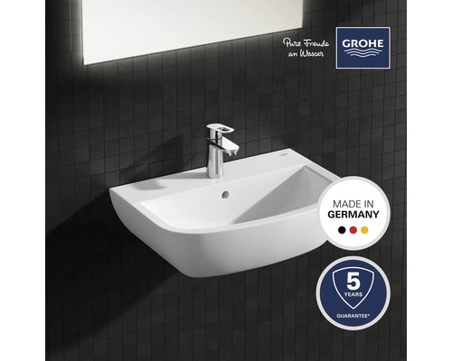 Keramische wastafel met kraan tegen een donkere tegelachtergrond, keurmerk Made in Germany, Grohe-logo, vijf jaar garantie
