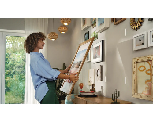 Vrouw houdt fotolijst voor een muur met al hangende lijsten om een nieuwe galerij te creëren.