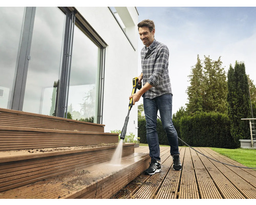 Man reinigt houten terras met hogedrukreiniger bij een huis