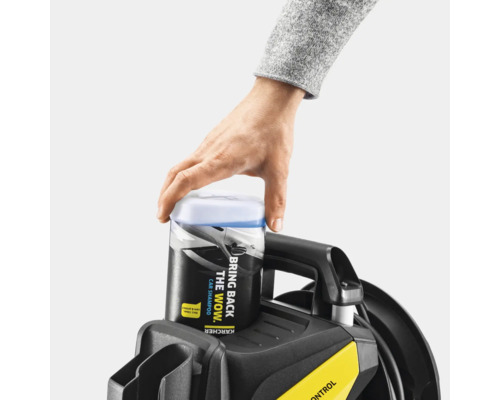 Een man plaatst een container autoshampoo op een hogedrukreiniger