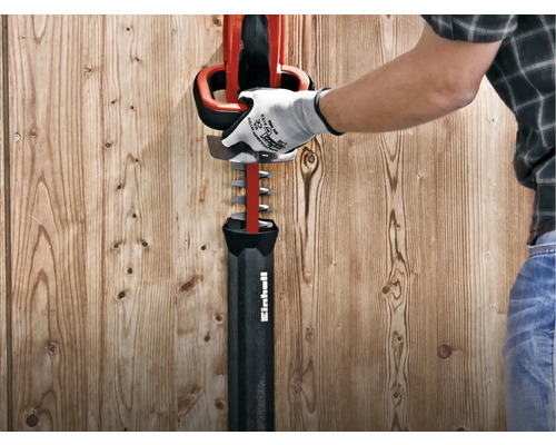 Een man met een handschoen inspecteert een rode heggenschaar van Einhell.