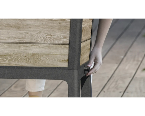 Gedetailleerd beeld van een verhoogde tuinbak van hout en metaal met een persoon die een knop bedient