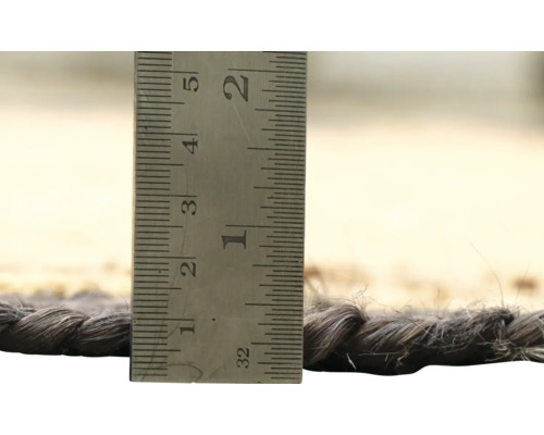 Detailopname van een tapijt met een meetinstrument om de dikte van het tapijt te bepalen.