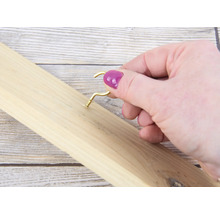 Een persoon schroeft een gouden haak in een houten plank