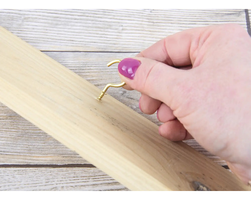 Een persoon schroeft een gouden haak in een houten plank