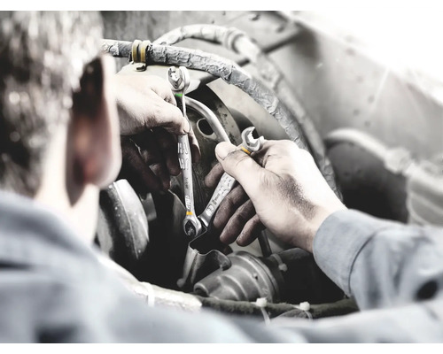 Een man werkt met twee moersleutels aan een motor.