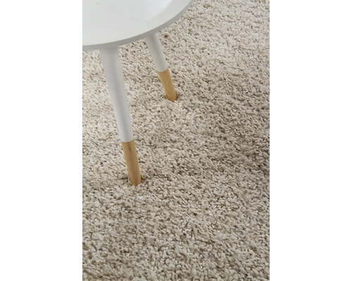 Detailopname van een beige hoogpolig tapijt naast een tafelpot.