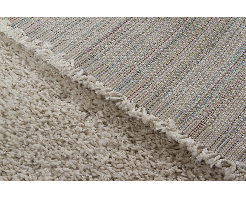 Detailopname van een beige tapijt met hoogpolig oppervlak en geweven achterkant