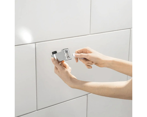 Persoon bevestigt een handdoekhaak aan een betegelde muur.