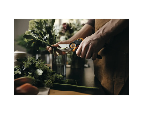 Een persoon knipt takken met een Fiskars tuinschaar op een tafel.