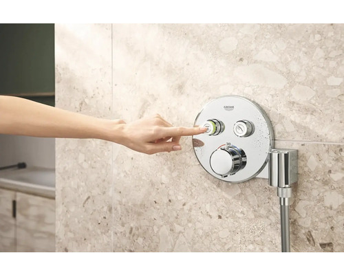 Een hand bedient een Grohe douchearmatuur aan een betegelde wand.