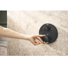 Een hand bedient een Grohe douchethermostaat op een betegelde wand