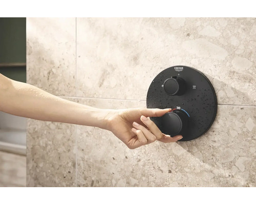 Een hand bedient een Grohe douchethermostaat op een betegelde wand