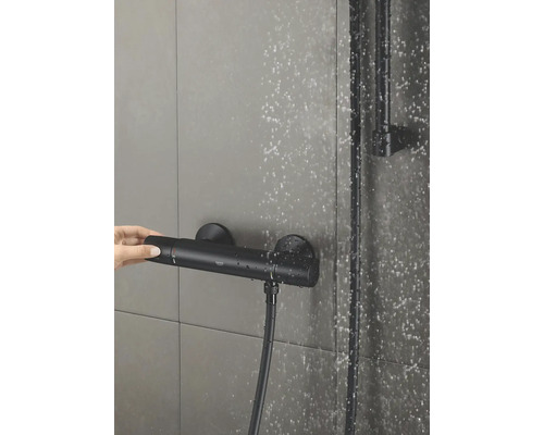 Foto van een thermostatische douchekraan met een hand die de temperatuurregelaar bedient.