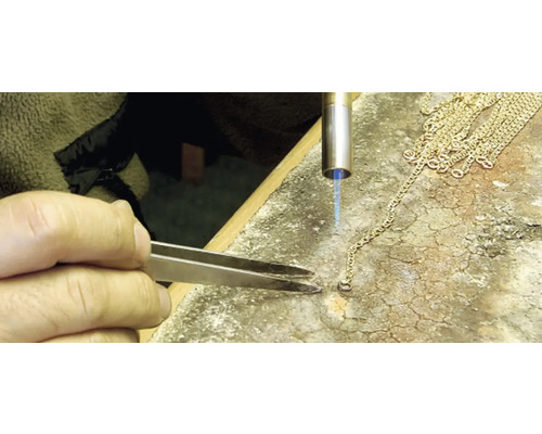 Close-up van een goudsmid die een gouden ketting bewerkt met een soldeerbout en een pincet.