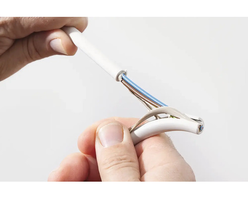 Close-up van een persoon die een witte elektrische kabel stript, waardoor de gekleurde binnengeleiders bloot komen te liggen.
