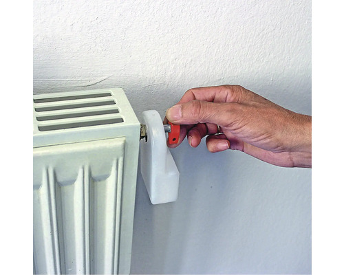 Een hand bedient een radiatorventiel op een radiator.