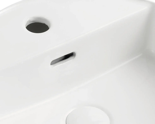 Gedetailleerde weergave van een witte wastafel met kraangat en overloop