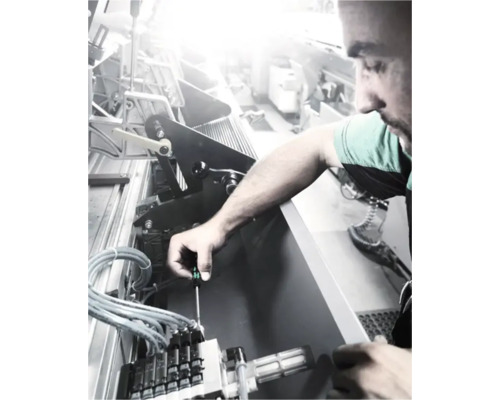 Een man repareert een machine met een schroevendraaier.