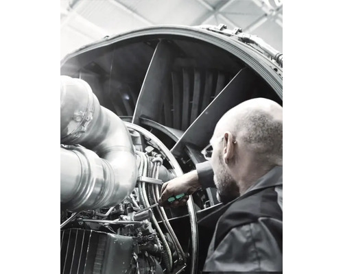 Een man inspecteert een vliegtuigmotor met een schroevendraaier.