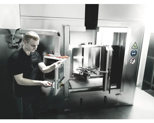 Een man bedient een industrieel reinigingsapparaat van metaal in een werkplaats.