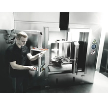 Een man bedient een industriële wasmachine in een werkplaats. Veiligheidstekens wijzen op mogelijke gevaren.