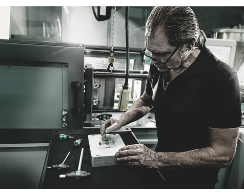 Een man werkt aan een werkstuk met schroevendraaiers in een werkplaats.